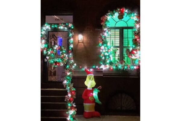 a photograph of a home decorated for Christmas with lights at nighttime, and a standing decoration of the Grinch.