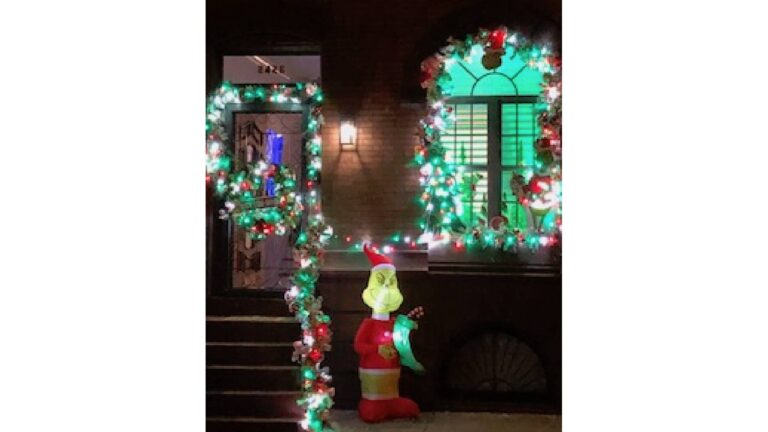 a photograph of a home decorated for Christmas with lights at nighttime, and a standing decoration of the Grinch.