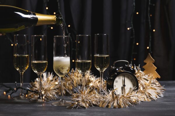 champagne glasses and bottle on a table with tinsel and an old fashioned alarm clock striking midnight