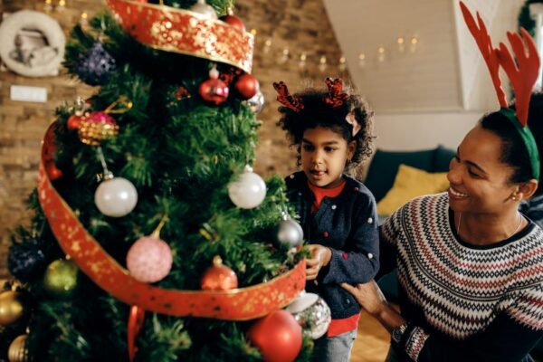 Black mother and young daughter decorating Christmas tree with ribbon and ornaments