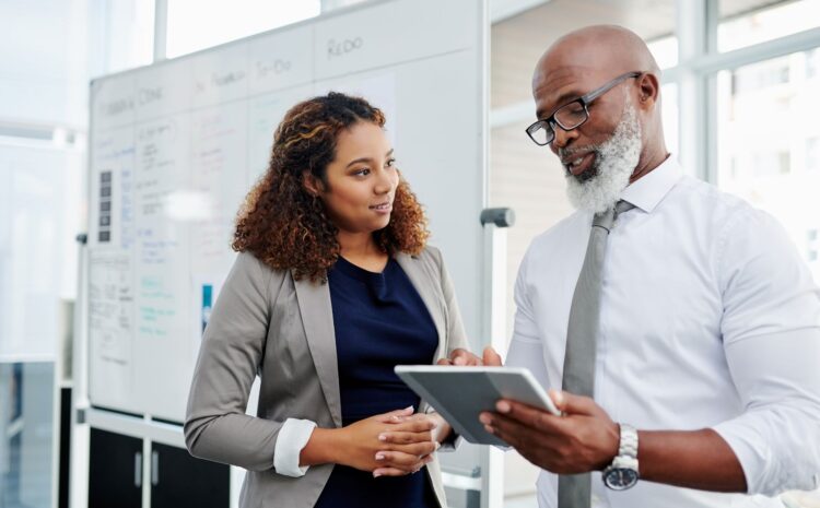 a mentor, an older African American man with gray bears, instructing mentee,  younger African American woman, at the office