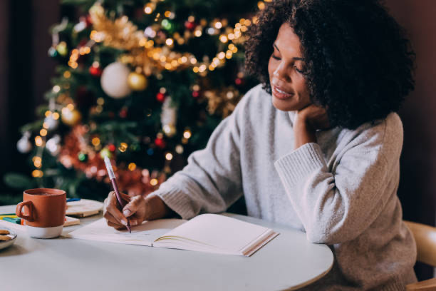 African American woman in front of Christmas tree writing down new year's resolutions