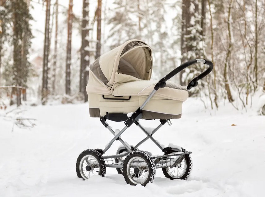 a baby carriage in the snow, in front of the woods