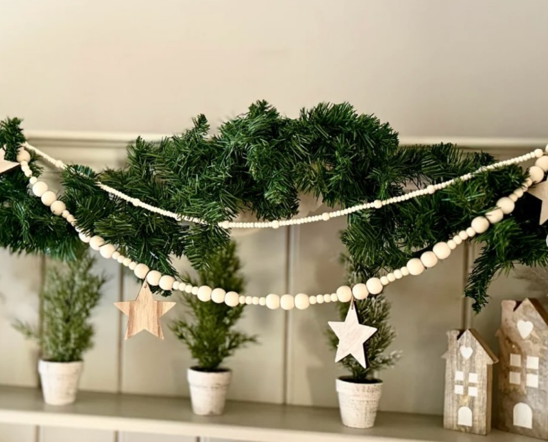 white beaded garland with hanging wooden stars wrapped around evergreen decoration on a shelf