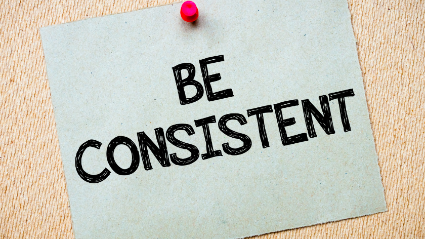 a piece of paper with the letters "Be Consistent" stuck on the bulletin board with tack