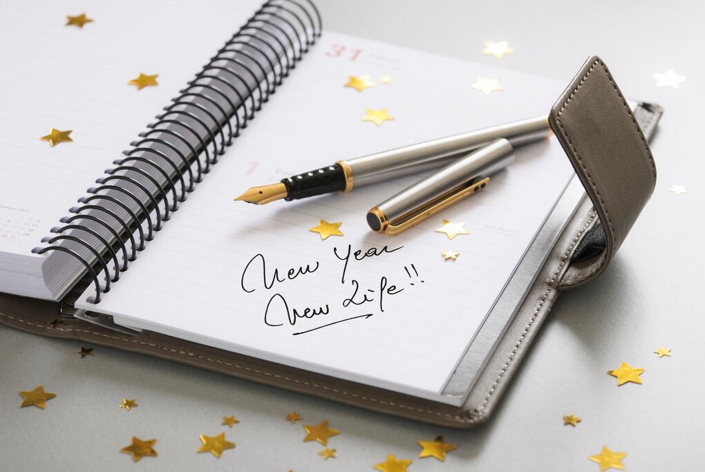 open notebook that has "New Year New Life!!" written in it, with star-shaped confetti and a silver fountain pen