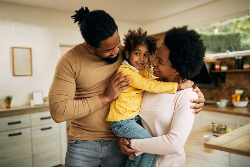 Happy African American father and mother holding young daughter in kitchen