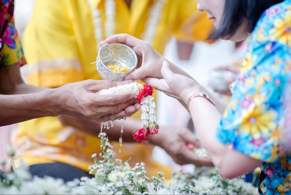 a pair of hands pouring water with flower petals on another person's hands holding a chain of flowers