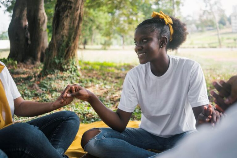 closeup of a Black woman smiling in a group of Black women holding hands sitting in a circle outdoors in a safe space
