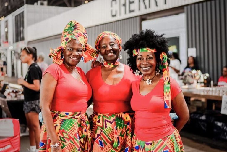three women in traditional African patterned skirts pose at an event