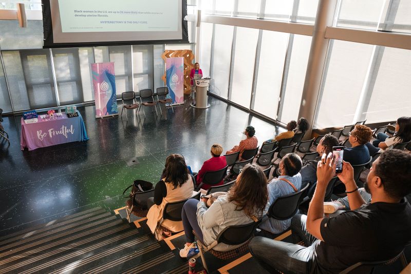 Presentation in auditorium set up for Barren Fruit, with a large screen, audience, and table of promotional material