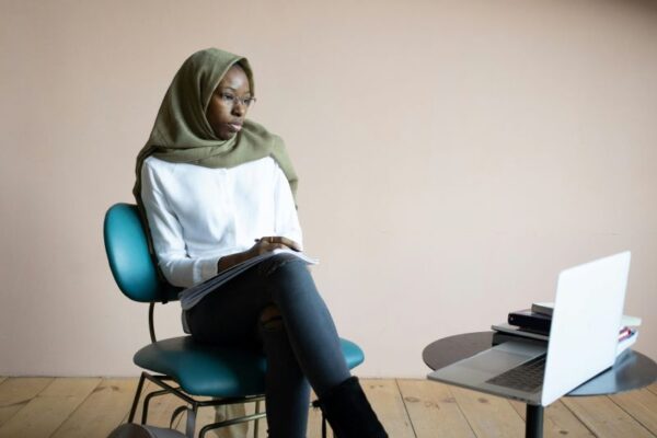 a Black hijabi woman carrying out an interview on a laptop