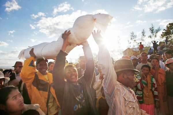 a group of locals carrying remains of the dead wrapped in sheets above their heads in celebration