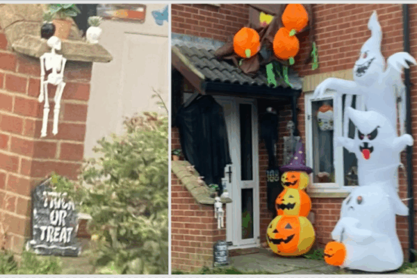 Halloween decorations in front of a house with hanging skeletons, a grave marker, stacked pumpkins, and ghosts