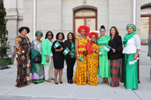 photo of Nigerian and African American ladies holding Nigerian flags and dressed in traditional and formal attire for the Nigeria Flag-Raising event in front of Philadelphia City Hall