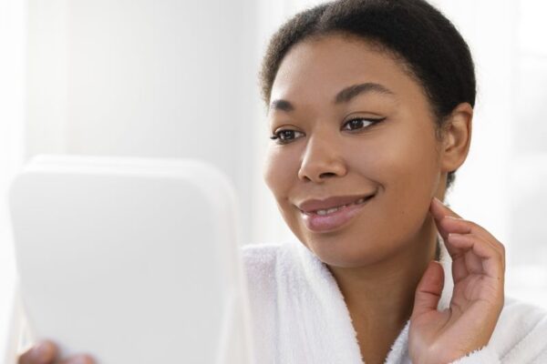 African American woman wearing a bathrobe, holding a mirror looking at her face