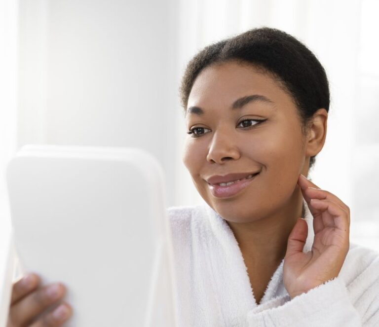 African American woman wearing a bathrobe, holding a mirror looking at her face