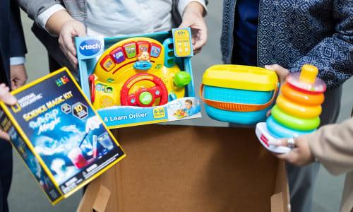 photo of hands holding toys for the toy drive, including a science kit and toddler's sensory toys