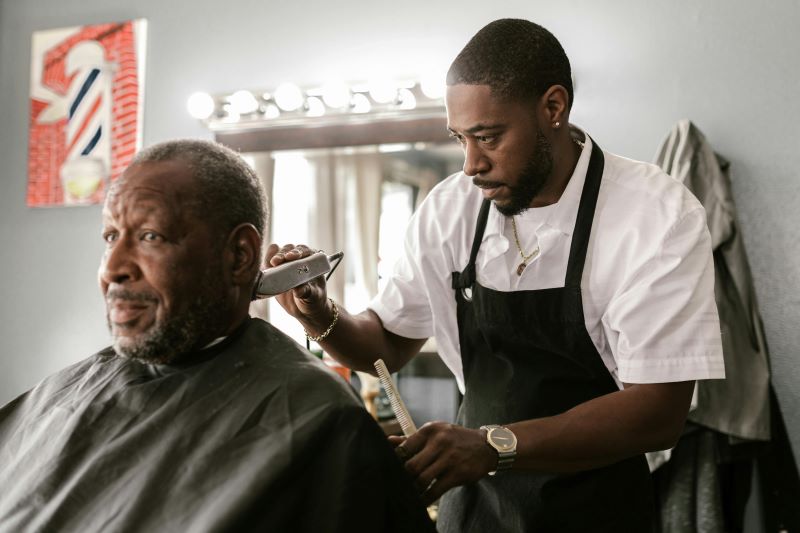 an African American barber trimming an older African American gentleman's hair