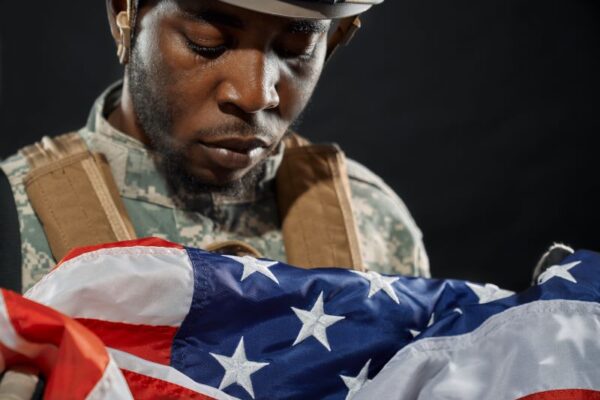 African American soldier in uniform holding and looking solemnly at American flag