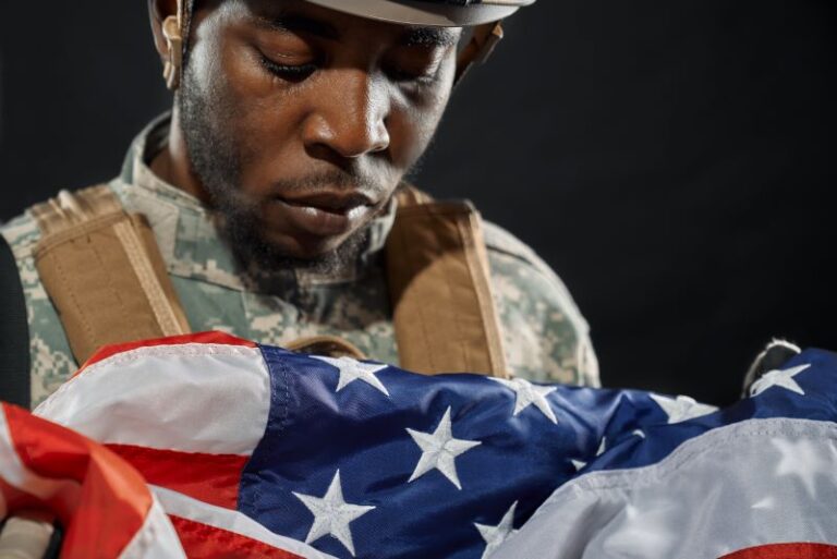 African American soldier in uniform holding and looking solemnly at American flag