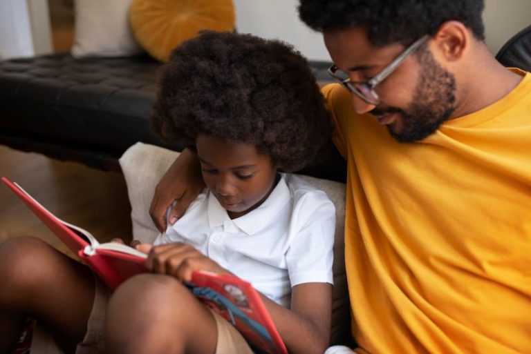 an African American child reading with his father in the living room