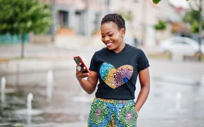 woman holding phone and smiling, in front of a fountain in the city