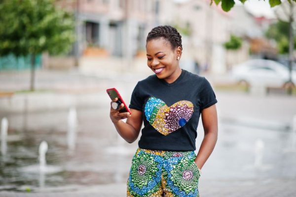 woman holding phone and smiling, in front of a fountain in the city