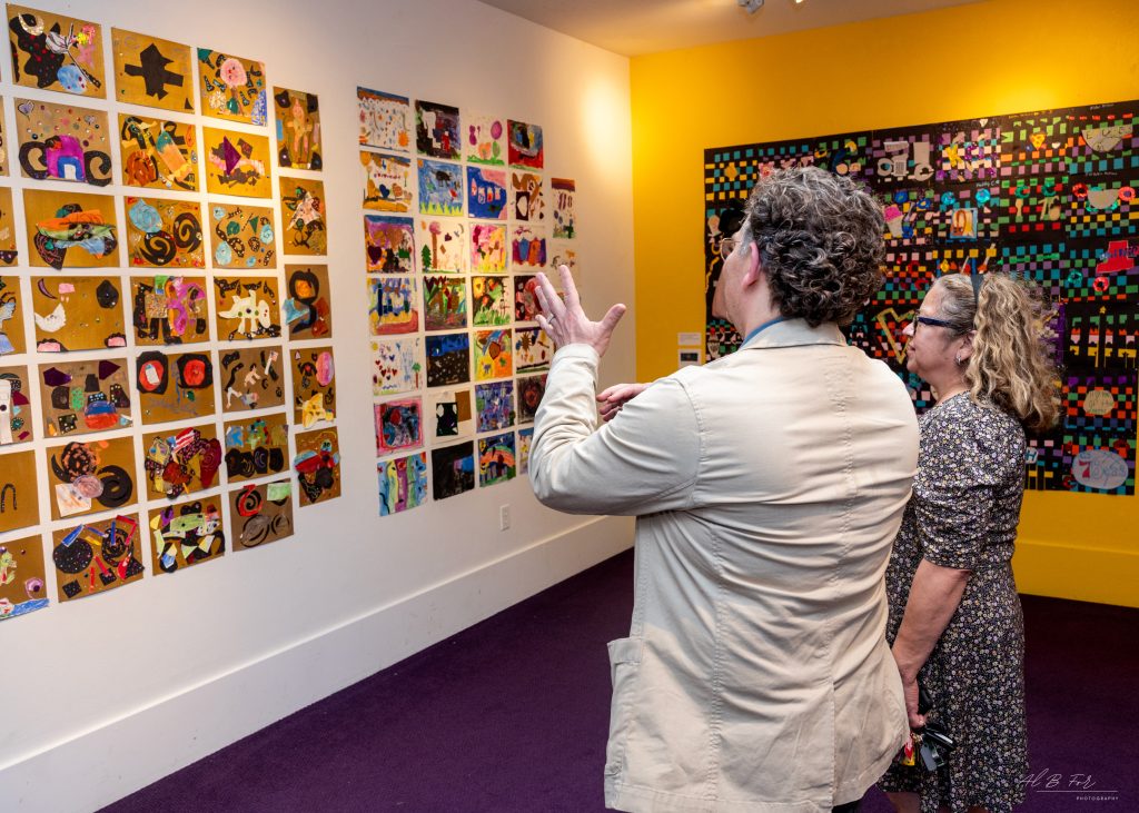 people standing in front of a wall of featured children's artwork