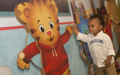 an African American toddler holding the hand of a wooden cutout of a cartoon tiger