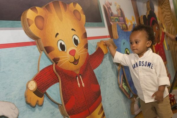 an African American toddler holding the hand of a wooden cutout of a cartoon tiger