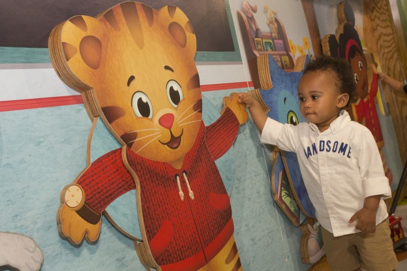 an African American toddler holding the hand of a wooden cutout of a cartoon tiger