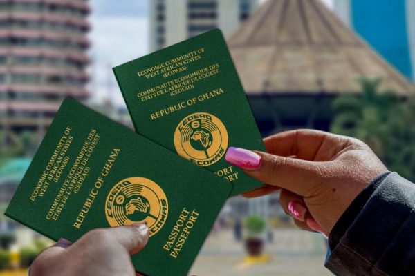 two hands holding Ghana passports in front of a cityscape