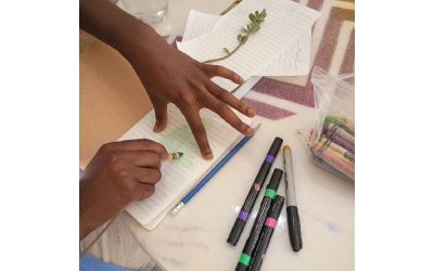 a pair of artist hands creating a crayon rubbing of a foliage at a table full of art supplies