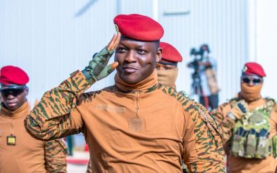 Ibrahim Traore in military hat and gear saluting. behind him are soldiers.