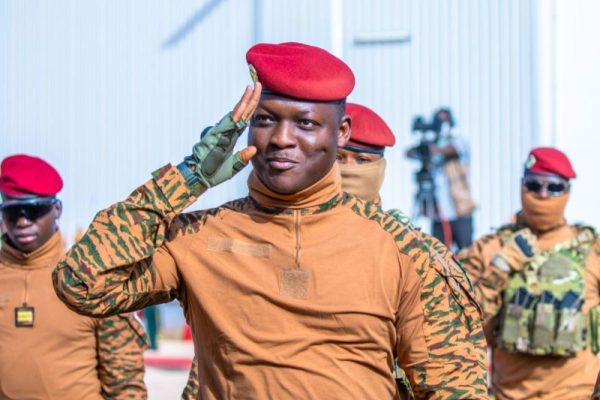 Ibrahim Traore in military hat and gear saluting. behind him are soldiers.