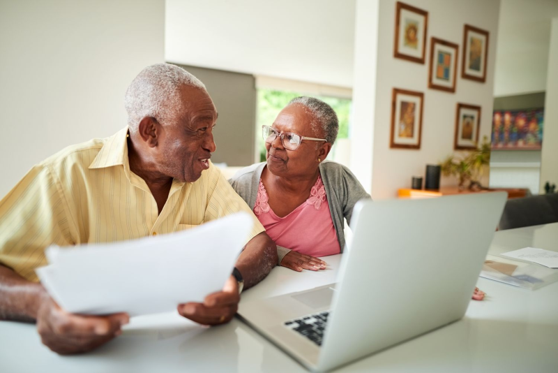 elderly couple discussing with an open laptop and paperwork